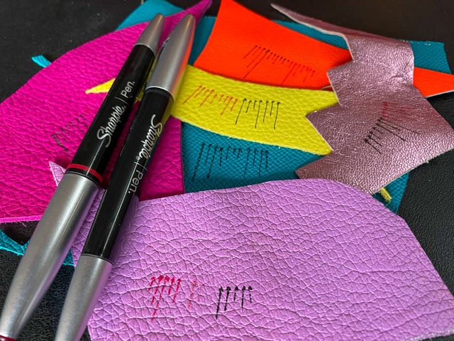 Two Sharpies on top of
multi-colored scraps of leather,
with little arrows drawn in black and red.