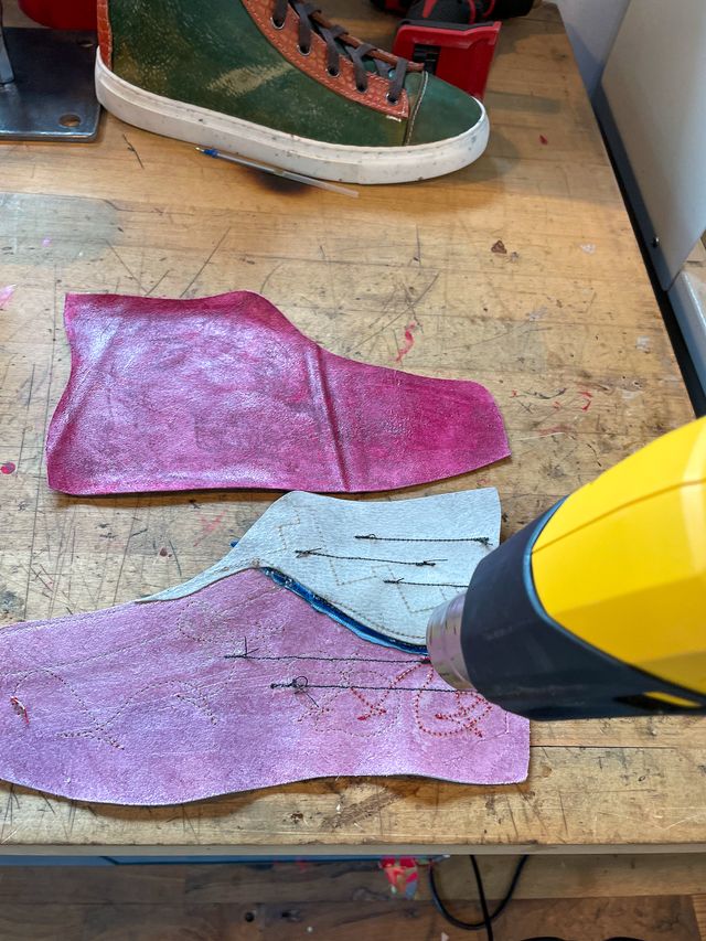 A heat gun setting glue on the backs of
a maroon leather high-top lining
and frankensteined low-high
with random stitches showing through.
