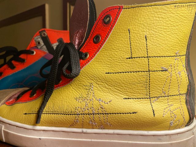 Closeup outside left shoe
in yellow leather with orange lace panel,
two tan-stitched close-wing moth sketches,
with black lines and arrows.