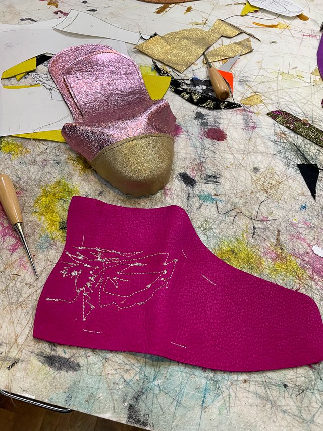 Scraps of paper and fabric on the work table,
two nested gold toe-caps sewn to rose gold tongues,
and a magenta high-top side panel
with a sketchy one-line stitched moth (wings spread),
and an awl for picking out remnants of stitched-in paper.