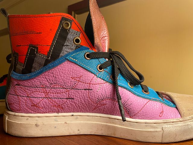 Closeup inside left shoe,
false low-top in lavender leather with
red scribbles, black lines and arrows,
blue lining and lace panels --
into silver/black stripes and orange upper.
