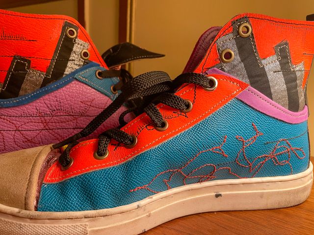Closeup inside right shoe,
false low-top in blue leather with
red scribbles, black lines and arrows, purple lining,
and orange lace panels --
into silver/black stripes and orange upper.